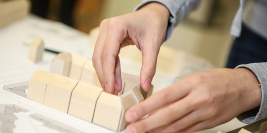 Zwei Hände stellen Bausteine auf, um ein Modell zusammenzusetzen.