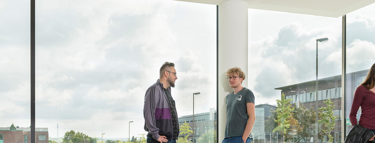 Studenten in Gesprächssituationen vor einer Fensterfront