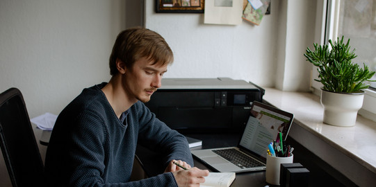 Lernen mit verschiedenen Medien Ein Student arbeitet mit Laptop und Notizbuch.