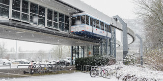 Eine H-Bahn steht an der an der H-Bahn-Haltestelle und die Straßen sind mit Schnee bedeckt.