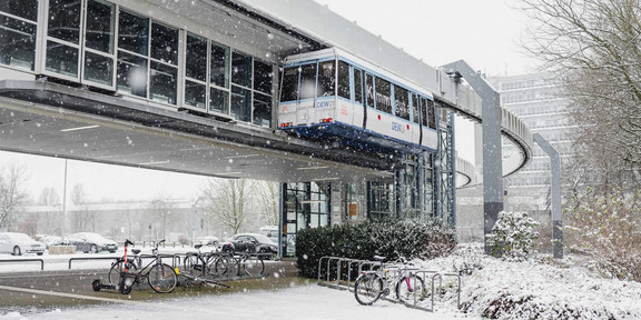 H-Bahn-Station im Schnee Eine H-Bahn steht an der an der H-Bahn-Haltestelle und die Straßen sind mit Schnee bedeckt.